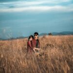 A young couple embraces in a peaceful hayfield, surrounded by golden grass under a bright blue sky.