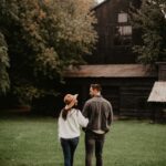 A couple walks through a grassy area towards a rustic barn, capturing a romantic autumn ambiance.