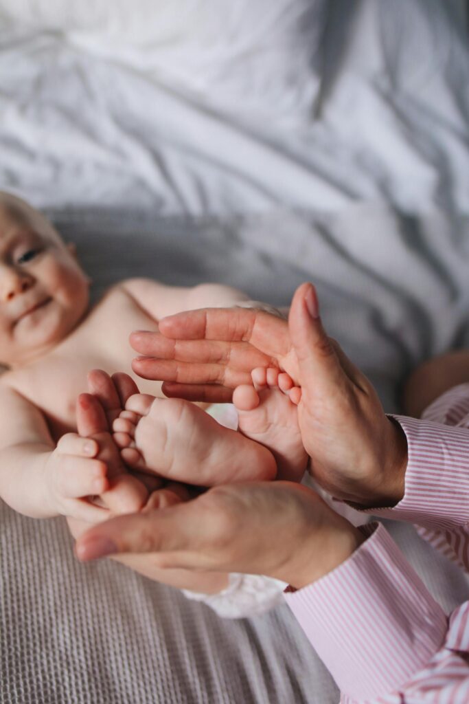 Close-up of a parent's hands gently holding a baby's feet indoors on a bed.
